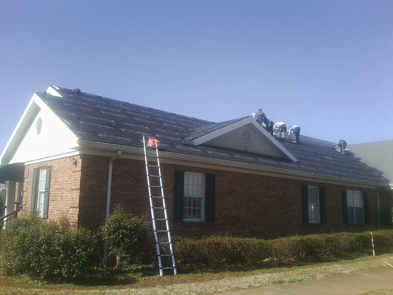 Crew tearing shingles off a brick ranch roof with a ladder set — Metal Roof Repair work by our crew in Annandale