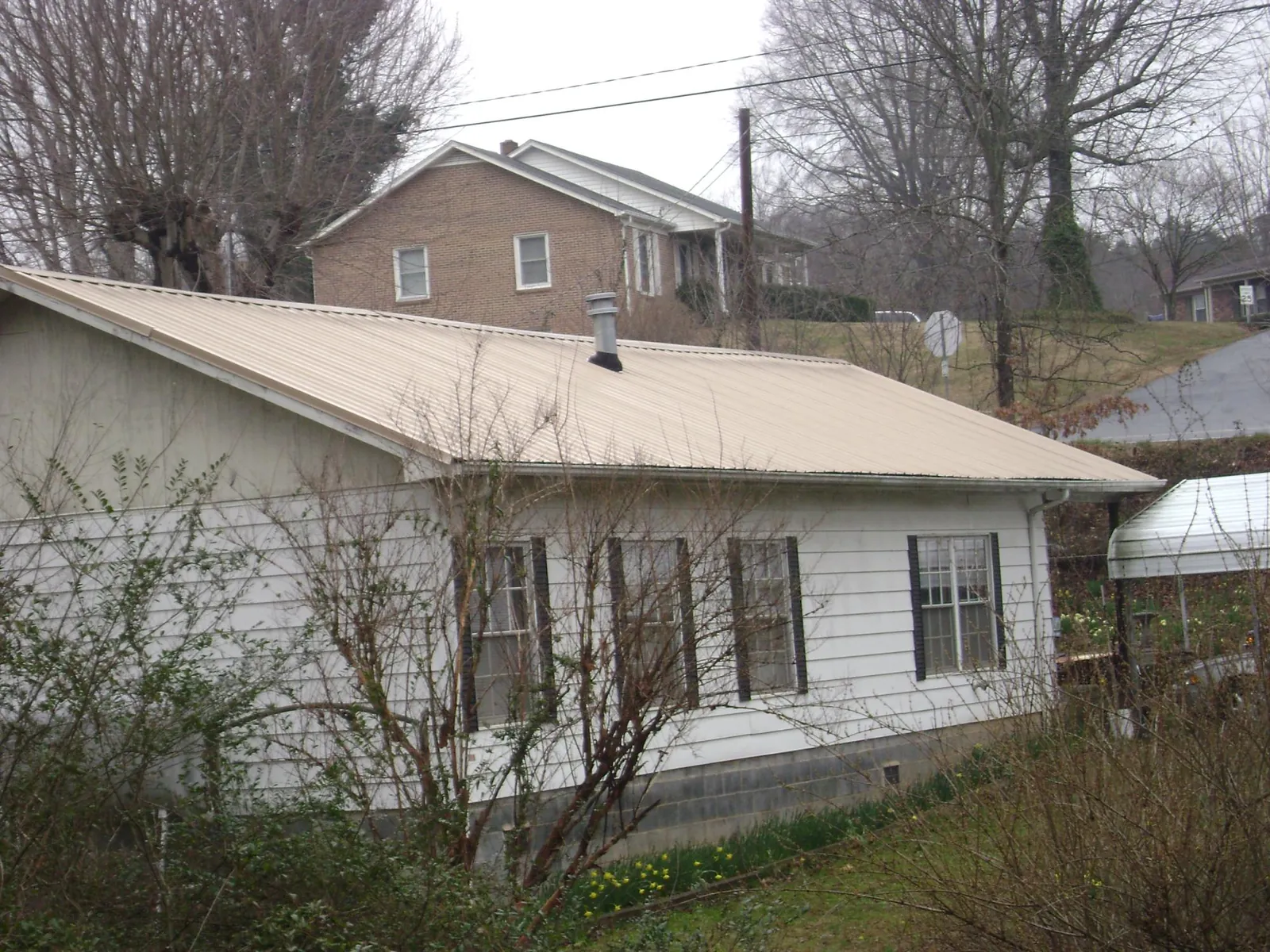 Tan metal roof on a white sided house set into a hillside — Commercial Roofing by Roofing Brothers in Annandale